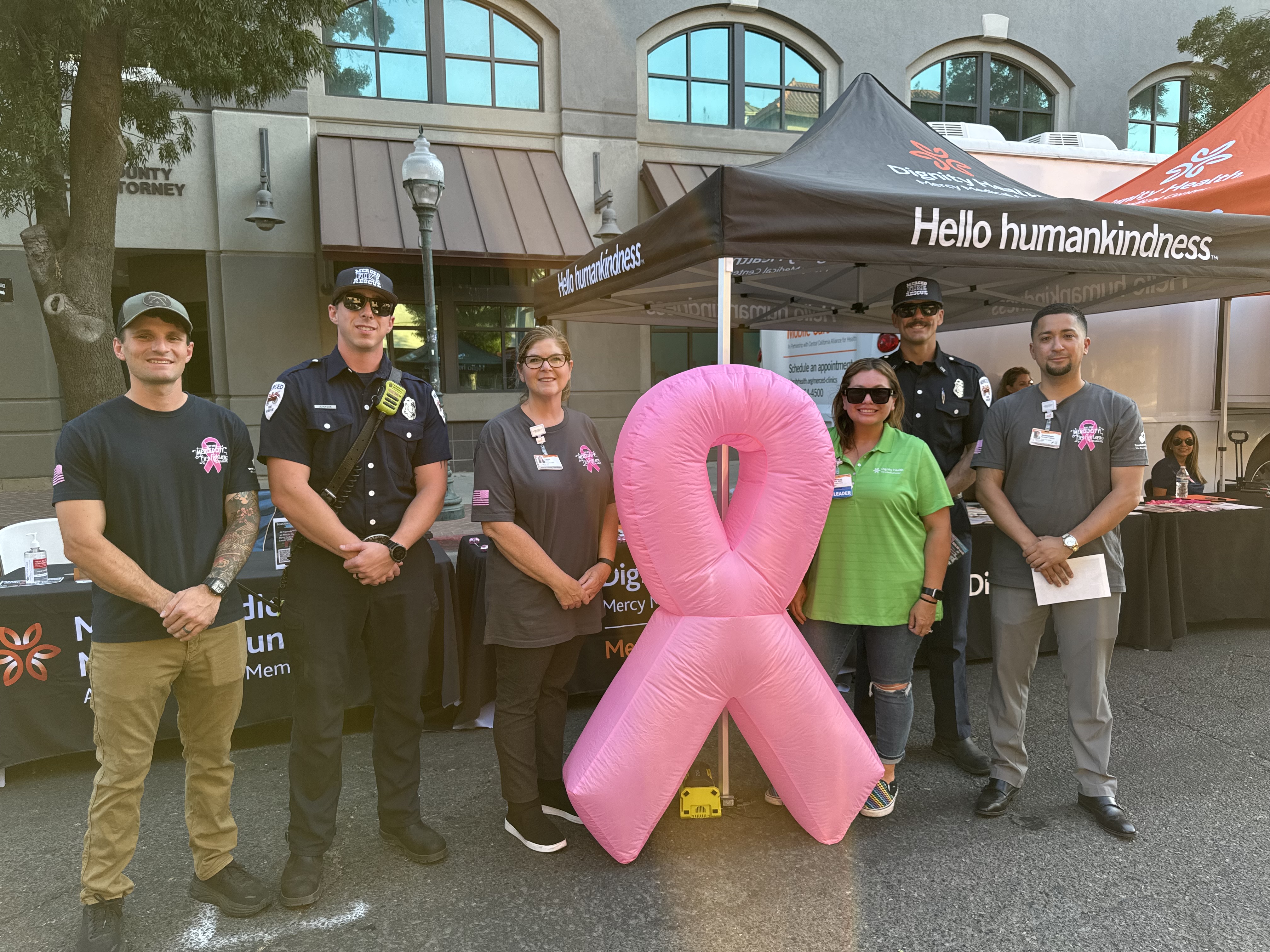 Firefighters stand at a booth with a pink ribbon balloon